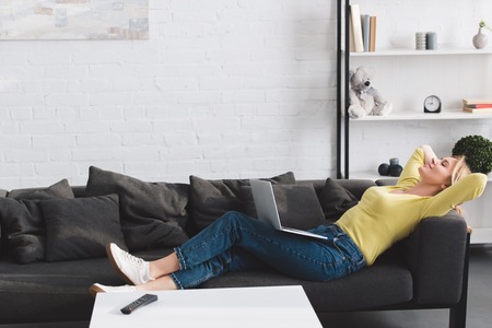 side view of happy relaxed woman lying with laptop on couchの写真素材