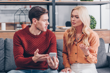 emotional young couple quarreling about smartphone at home, jealousy conceptの写真素材