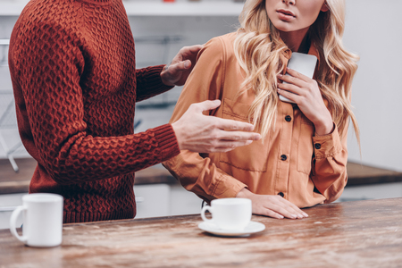 cropped shot of man quarreling with girlfriend holding smartphone in kitchen, distrust conceptの写真素材