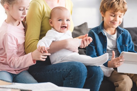 cropped shot of mother with infant child and cute siblings sitting together in sofaの写真素材