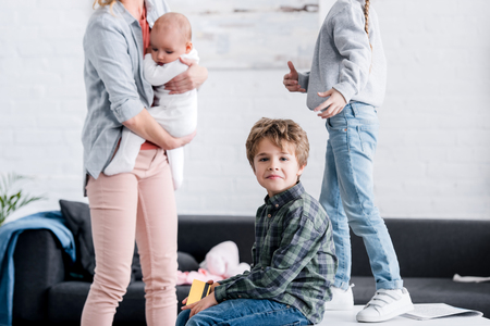 little boy holding credit card and looking at camera while sister and mother with infant child standing behindの写真素材
