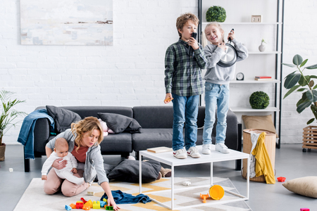exhausted mother with infant child sitting on floor while naughty kids playing at homeの写真素材