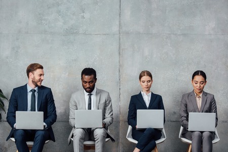 multiethnic businesspeople sitting on chairs and using laptops in waiting hall