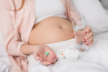 Partial view of pregnant woman holding medicine and glass of waterの写真素材