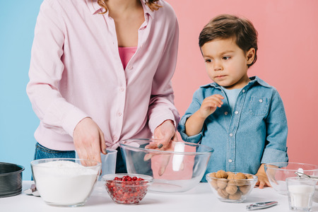 cute little boy with mother preparing ingredients for baking on bicolor background