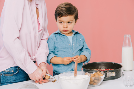 cute little boy helping mother cracking walnuts while cooking together isolated on pinkの写真素材