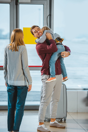 happy father holding in arms daughter near wife in airportの写真素材
