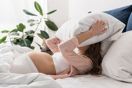 Pregnant woman lying in bed and holding pillow on headの写真素材
