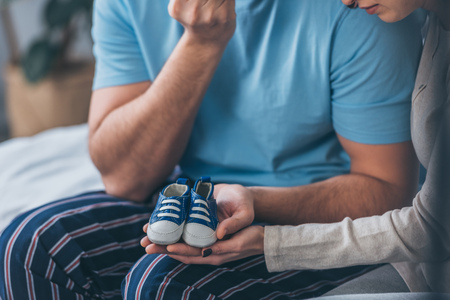 cropped view of parents holding baby shoes at homeの写真素材