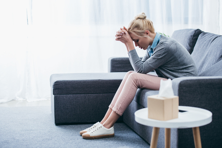depressed woman with folded hands sitting at home on couchの写真素材