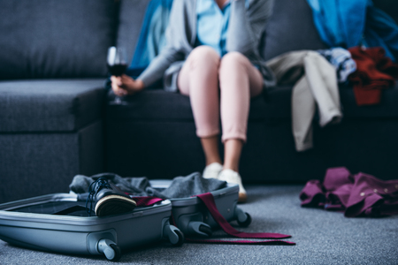 cropped view of woman sitting with glass of red wine while packing in living room after breaking up with boyfriendの写真素材