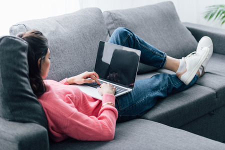 indian woman using laptop with blank screen while lying on sofaの写真素材