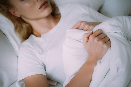 cropped view of woman in white pajamas lying in bed and holding blanketの写真素材