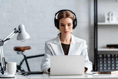 serious businesswoman in headphones sitting at computer desk at workplaceの写真素材