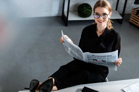 beautiful businesswoman in black clothes and glasses sitting at table and smiling at cameraの写真素材