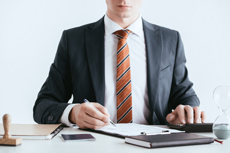 cropped view of  man in suit holding pen near document isolated on white