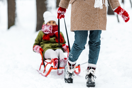 cropped view of mother pulling daughter in warm clothing on sledge in winter parkの写真素材