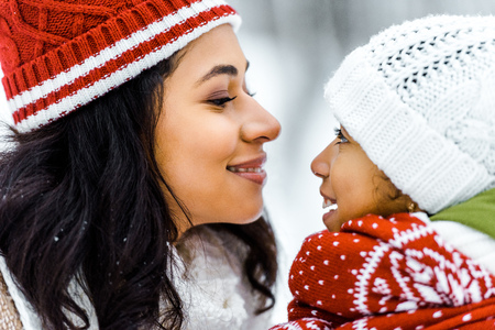 attractive african american mother smiling and looking at cute preteen daughter in winter forestの写真素材