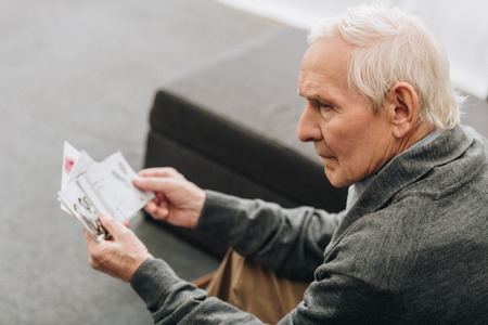 sad retired man with grey hair looking at old photos at homeの写真素材