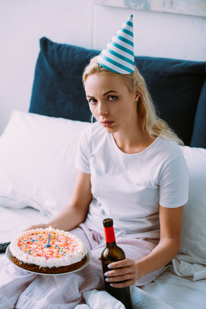 upset woman with bottle of wine and cake celebrating birthday in bed aloneの写真素材