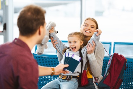 selective focus of cheerful daughter holding hands above head and smiling with mother near father with passports with ticketsの写真素材
