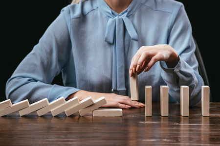 partial view of woman sitting and picking wooden brick from row of blocks on desk isolated on black