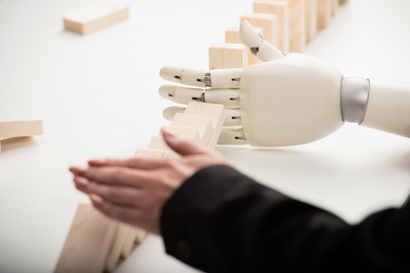 cropped view of woman pushing wooden bricks while robotic hand preventing row from falling