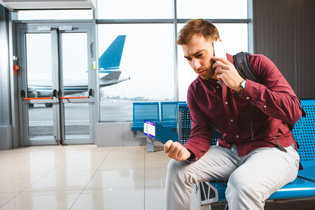 man talking on smartphone while sitting in waiting hallの写真素材