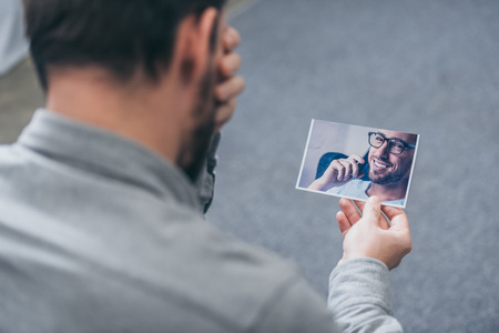 cropped view of man sitting and looking at photo with man at home, grieving disorder conceptの写真素材
