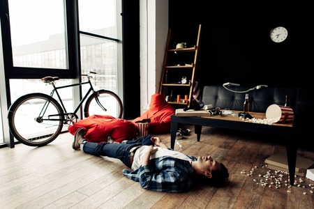 drunk man lying on floor in messy living room after partyの写真素材
