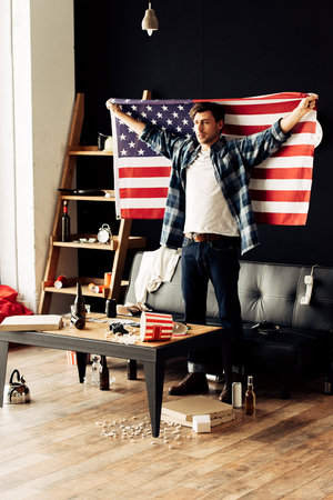 handsome man holding american flag in messy living roomの写真素材