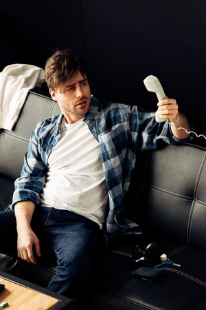 drunk man looking at retro phone and sitting on sofa after party at home