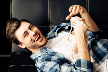 cheerful man holding bra while lying on sofa after partyの写真素材