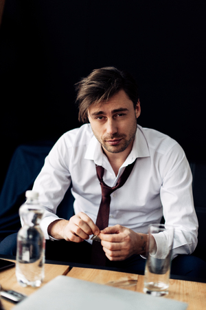 tired businessman holding pill in hands near glass of water after partyの写真素材