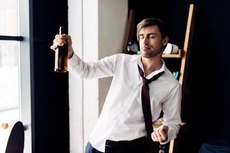 drunk man with closed eyes showing winner sign and holding bottle in hand after partyの写真素材