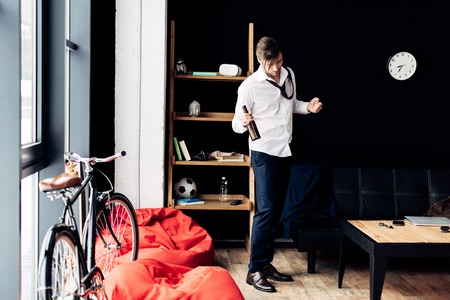 sleepy man in suit showing winner sign and holding bottle in hand after partyの写真素材