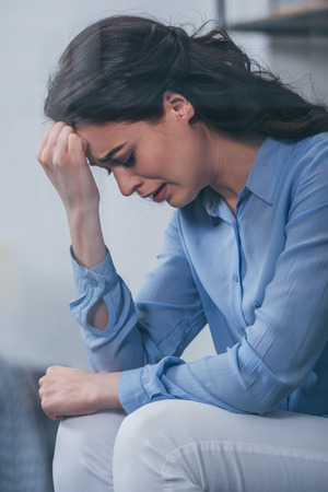 upset woman having headache, grieving and crying at homeの写真素材