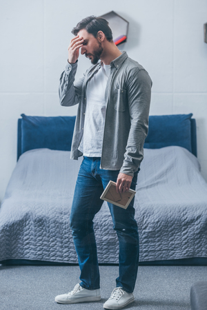 man holding photo frame, grieving and having headache in bedroomの写真素材