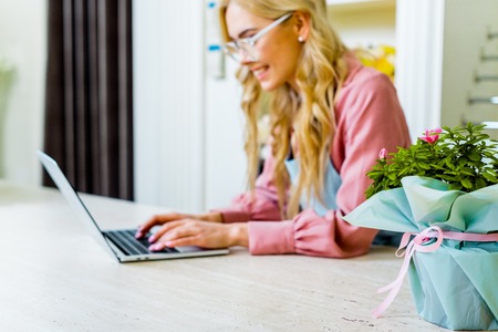 selective focus of floral bouquet with female florist using laptop in flower shop on backgroundの写真素材