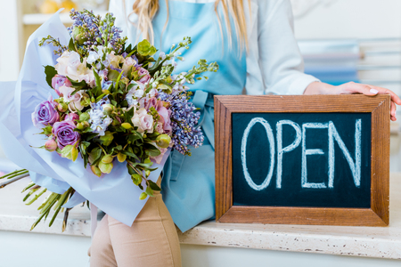 cropped view of female flower shop owner holding chalkboard with 'open' lettering and colorful bouquetの写真素材