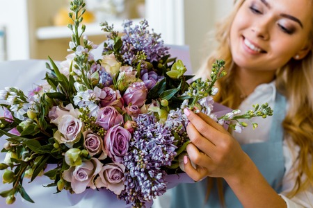 smiling female florist arranging bouquet with lilac and roses in flower shopの写真素材