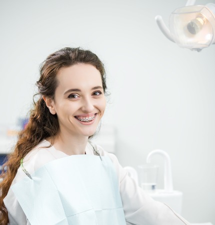 cheerful woman with braces on teeth smiling in dental clinicの写真素材