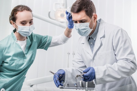 female dentist in mask standing near colleague holding dental instrumentsの写真素材
