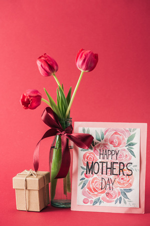 happy mothers day greeting card, bouquet of red tulips with red satin bow, and gift box on red backgroundの写真素材