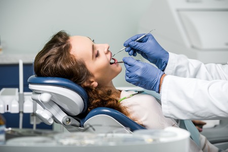 cropped view of dentist in latex gloves examining teeth of woman in dental clinicの写真素材