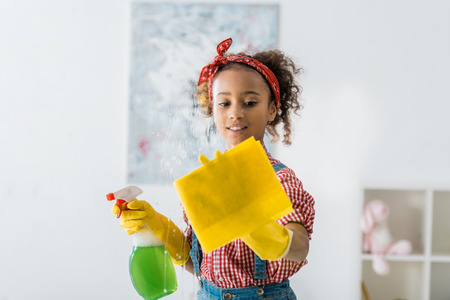cute african american child holding yellow rag and green spray bottleの写真素材