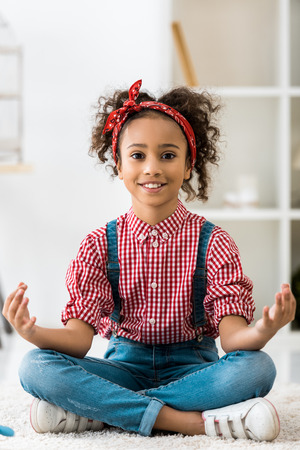 smiling african american child sitting in lotus pose and looking at cameraの写真素材