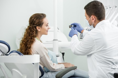 dentist in mask and latex gloves pointing with finger at x-ray of teeth near patientの写真素材