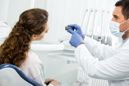 selective focus of dentist in mask pointing with finger at x-ray of teeth near patientの写真素材