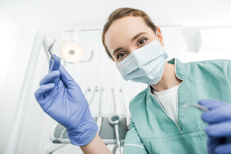 selective focus of female dentist in latex gloves and mask holding dental instrumentsの写真素材